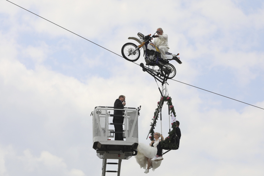 Pastor Stefan Gierung, left, stands in a cage atop of a fire service ladder in front of bride Nicole Backhaus, center, and groom Jens Knorr, right, both sitting in a swing dangling under a motorcycle with artist Falko Traber, top, during the wedding ceremony atop a tightrope in Stassfurt, Germany, on Saturday.