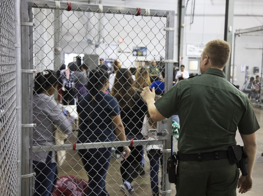 A U.S. Border Patrol agent watches as people who’ve been taken into custody related to cases of illegal entry into the United States, stand in line at a facility in McAllen, Texas, on Sunday. (U.S.