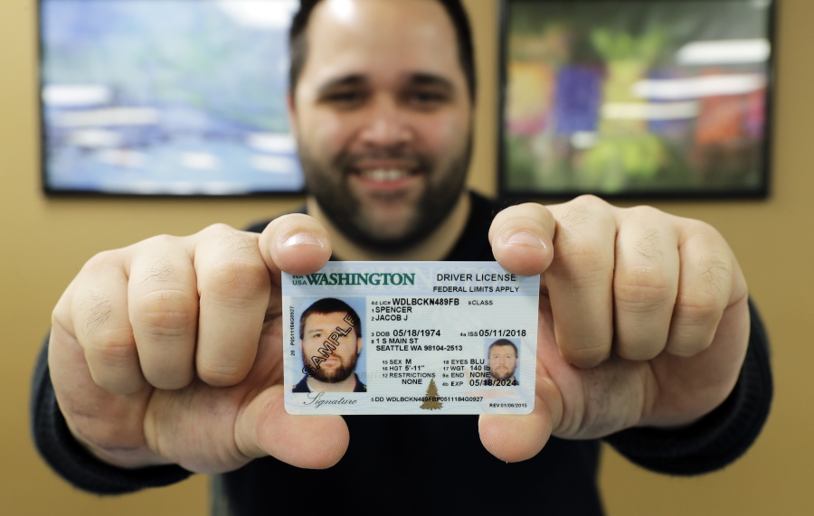 Ryan Norris, a license service representative at the Washington state Dept. of Licensing office in Lacey, Wash., poses for a photo Friday while holding a sample copy of a Washington drivers license. Some Washington licenses and identification cards will soon be marked with the words “federal limits apply” as the state moves to comply with a federal law that increased rules for identification needed at airports and federal facilities. (AP Photo/Ted S.