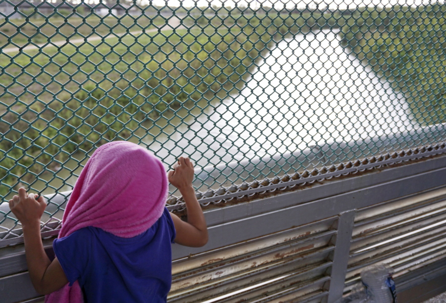 Five-year-old Genesis of La Ceiba, Honduras, peers through fencing Saturday along Gateway International Bridge over the Rio Grande River that connects Brownsville, Texas, with Matamoros, Mexico, as her family seeks asylum in the U.S.
