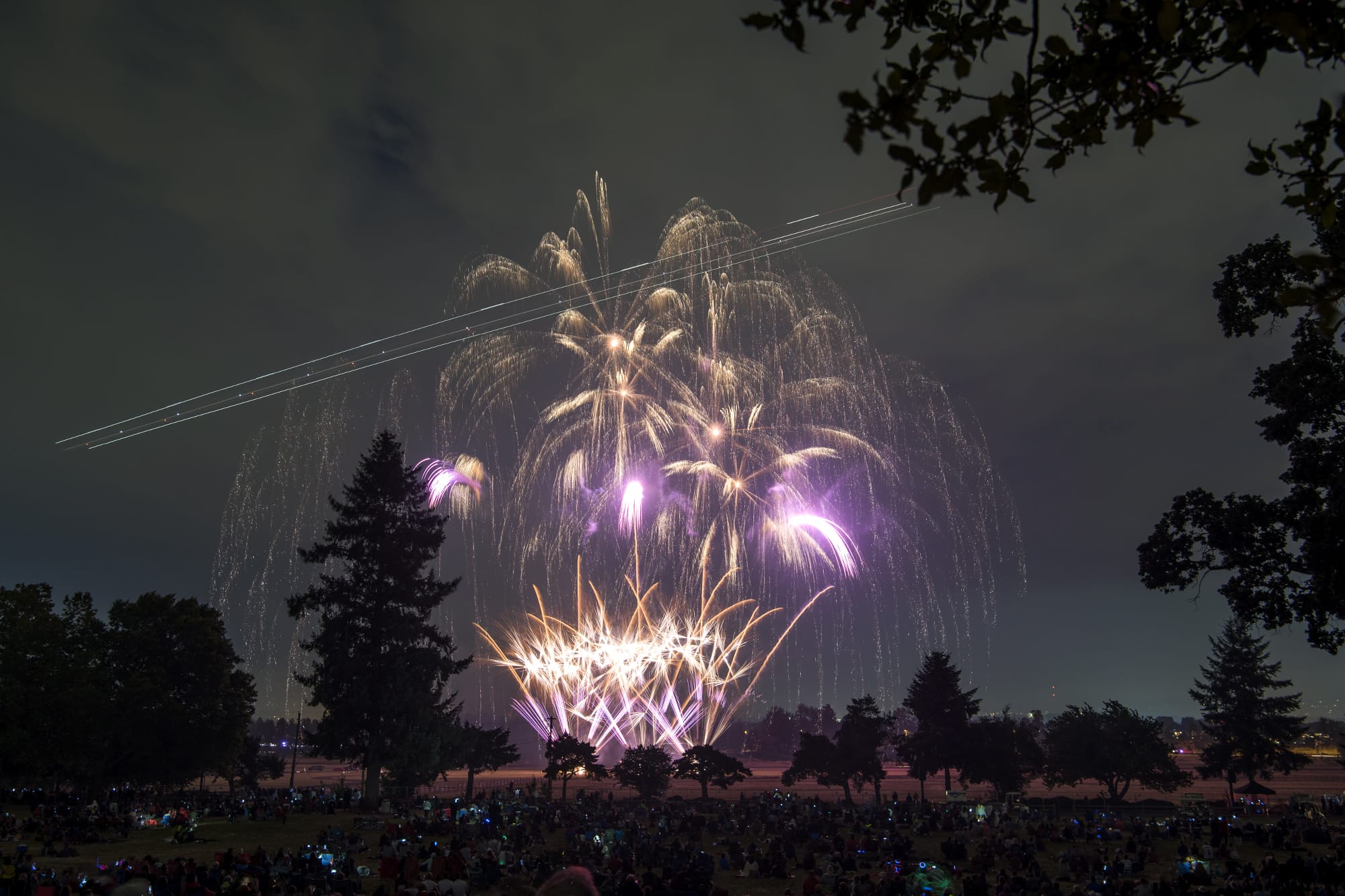 The lights of an airplane streak through fireworks as they light the night sky above Fort Vancouver National Historic Site and Pearson Field on Wednesday evening.