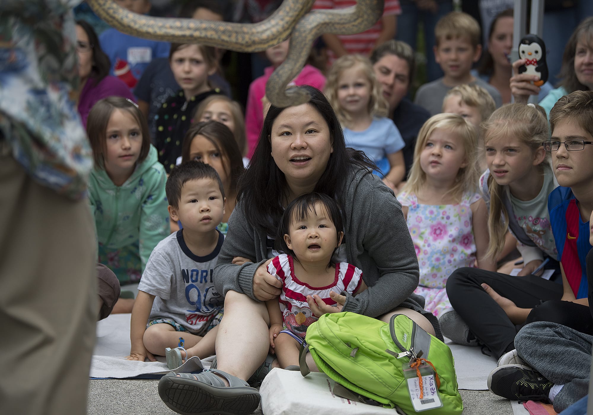 LEADOPTION Young Zhang, 3, front row from left, his mom, Megan Chan, and his sister, Xia Zhang, 2, get a front row seat to view an anaconda while joining a crowd of reptile fans during a presentation by The Oregon Reptile Man, Richard Ritchey, at Three Creeks Community Library on Thursday morning, July 19, 2018. The event was part of the library's summer reading program.