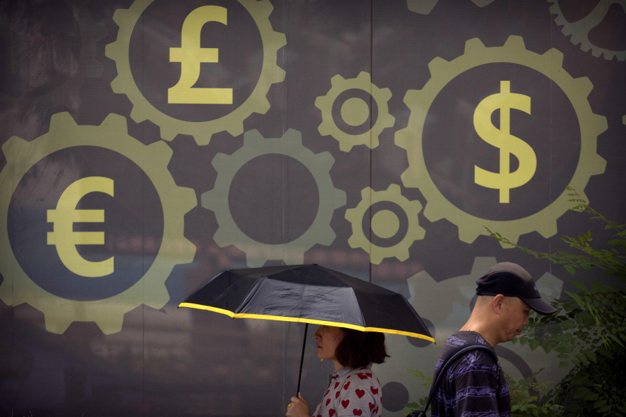 People walk past a mural displaying world currency symbols on the outside of a bank in Beijing, Friday, July 20, 2018. China’s central bank is allowing its tightly controlled yuan to drift lower against the dollar, a move that could help exporters cope with U.S. tariff hikes but raises the risk of reigniting an outflow of capital Beijing spent months trying to stanch.