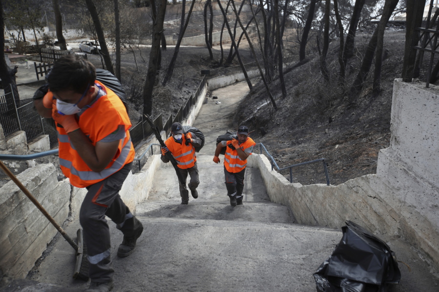 Workers carry bags with debris as clean-up operations get underway following a deadly wildfire in Mati, east of Athens, on Thursday. Rescuers intensified a grim house-to-house search Wednesday for more casualties from a deadly forest fire outside Athens, as the country’s military said it was using footage from U.S. combat drones and surveillance aircraft to try to determine whether arsonists were behind the blaze and stop future attacks.