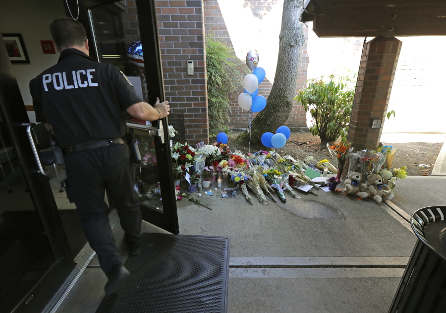 A police officer walks past flowers and other tributes honoring Kent Police Officer Diego Moreno on Monday. Moreno died Sunday after being hit by a fellow officer in a patrol car that was chasing a fleeing suspect. (Ted S.