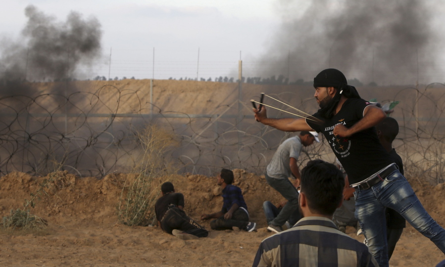 A protester hurls stones while others take cover Friday near the fence of the Gaza Strip border with Israe during a protest east of Khan Younis, southern Gaza Strip.