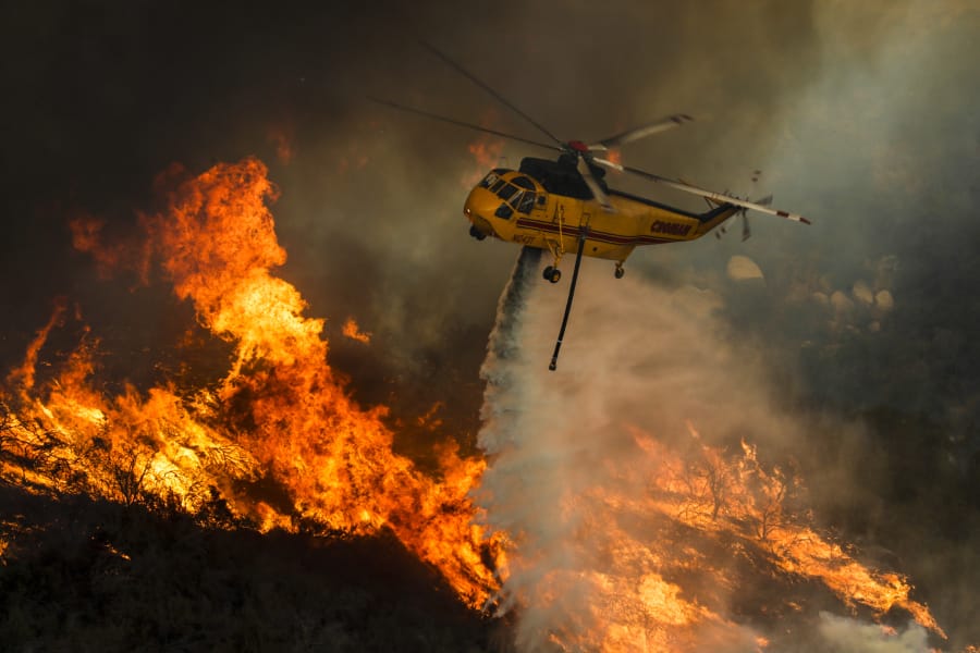A helicopter drops water Friday on raging flames of the Holy Fire along Ortega Highway in Lake Elsinore, Calif. The fire is only 5 percent contained and is one of 20 burning around the state.