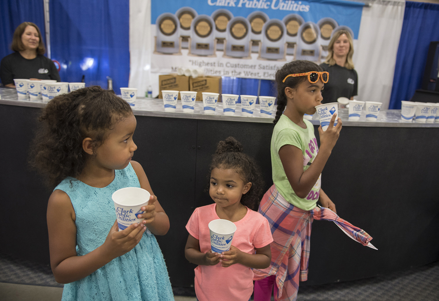 Janaye Bol, 6, of Graham, left in blue, escapes from the heat with a cold cup of water with her sisters, Adrienne, 4, and Mackensie, 9, at the Clark Public Utilities booth at the Clark County Fair on Thursday afternoon. Janaye said she was having a good time at the fair despite the heat and appreciated having the free fans and water to cool off.