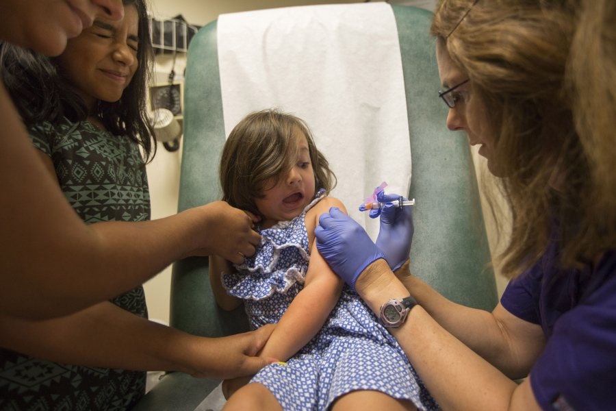 Abigail Crumrine, 4, gets an injection from Kris Black, right, on Wednesday at the Free Clinic of Southwest Washington. Abigail gets support from her sister, Mary, second from left.