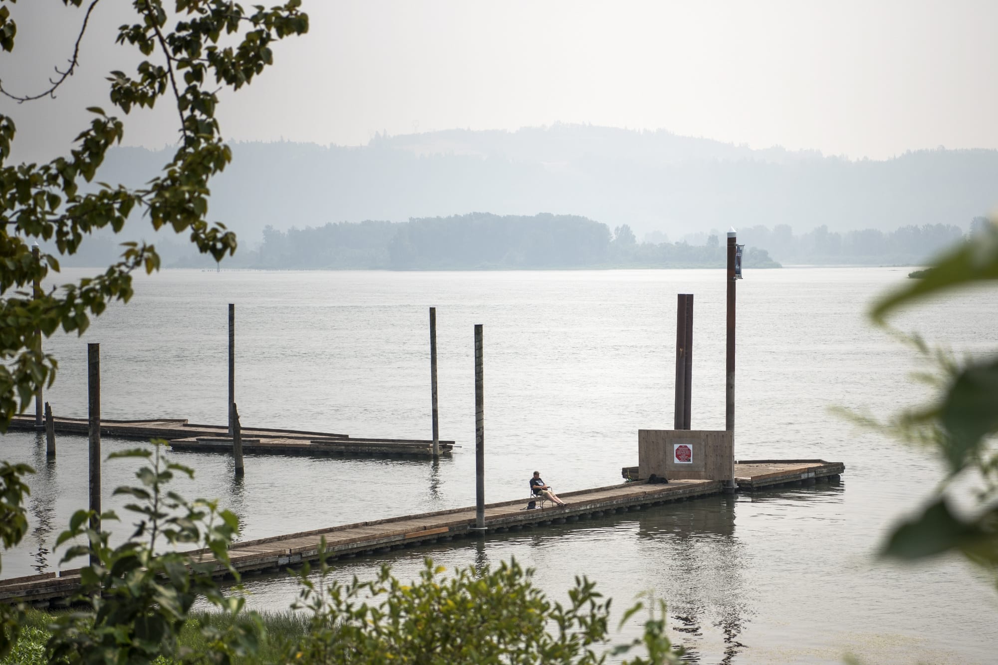 Randy Rolene of Vancouver relaxes with his dog, Bella, and fishes off of the dock at Steamboat Landing Park in Washougal on Tuesday. Rolene said he decided to come out to the river to take his dog for a swim, but he'll probably head home early because of the smoke. "It's nasty," he said.