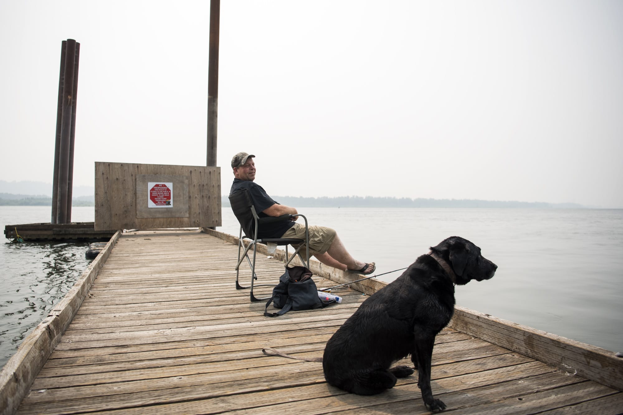Randy Rolene of Vancouver relaxes with his dog Bella and fishes off of the dock at Steamboat Landing Park in Washougal on Tuesday, Aug. 14, 2018. Rolene said he decided to come out to the river to take his dog for a swim, but he'll probably head home early because of the smoke. "It's nasty," he said.