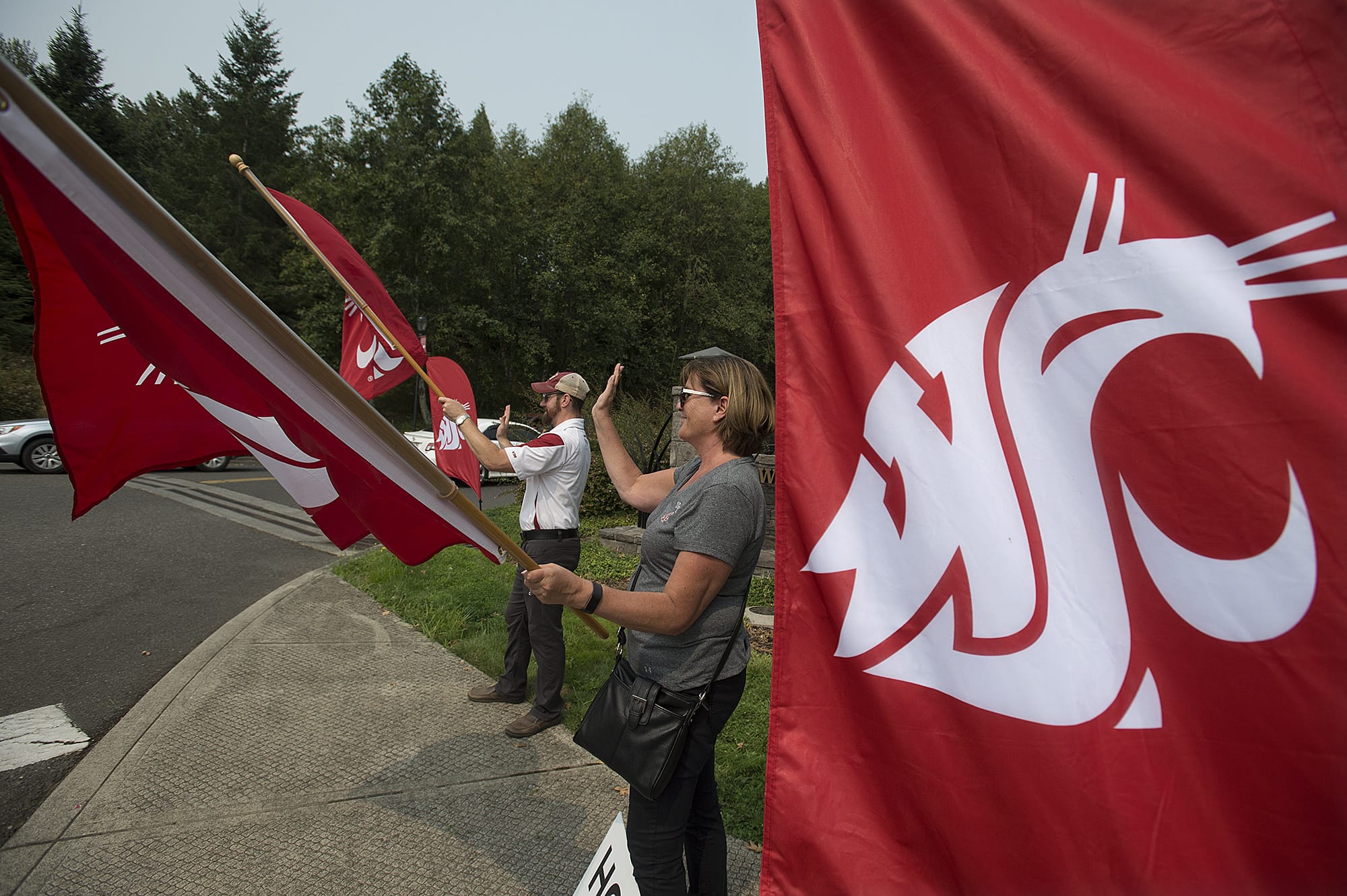 Lisa Abrahamsson, assistant director of development and alumni relations, joins Erich Orth of the class of 1999 to wave the Washington State University banner on Monday morning at Washington State University Vancouver. Dozens of WSU staff, alumni and friends turned out for the daylong ritual. Held on the first day of classes, the volunteers took hourlong turns standing on three street corners leading to the Salmon Creek campus, welcoming new and returning students.