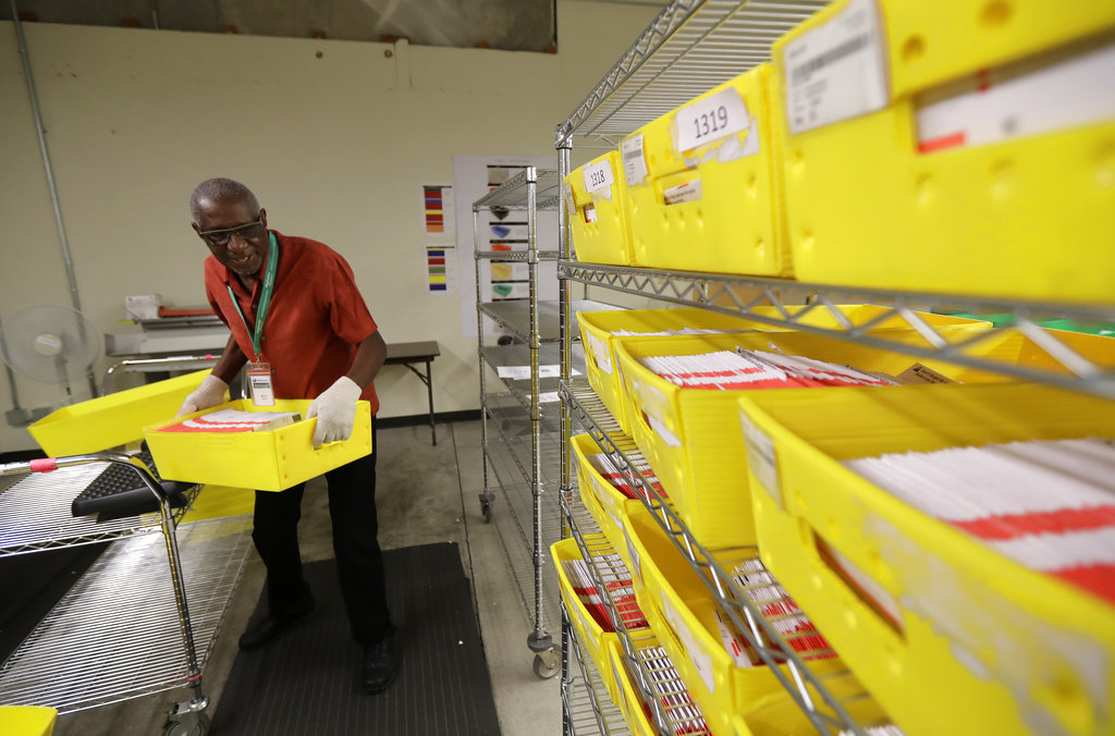 Marvin McKinly stacks ballots from Washington state's primary election on racks after they were run through a sorting machine, Tuesday, Aug. 7, 2018, at King County Election headquarters in Renton, Wash. Voters will decide which candidates advance to the November ballot in 10 congressional races, a U.S. Senate seat and dozens of legislative contests. (AP Photo/Ted S.