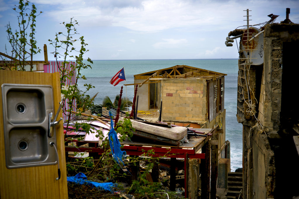 FILE - In this Oct. 5, 2017 file photo, a Puerto Rican national flag is mounted on debris of a damaged home in the aftermath of Hurricane Maria in the seaside slum La Perla, San Juan, Puerto Rico. An independent investigation ordered by Puerto Rico’s government estimates that nearly 3,000 people died as a result of Hurricane Maria. The findings issued Tuesday, Aug. 28, 2018, by the Milken Institute School of Public Health at George Washington University contrast sharply with the official death toll of 64.