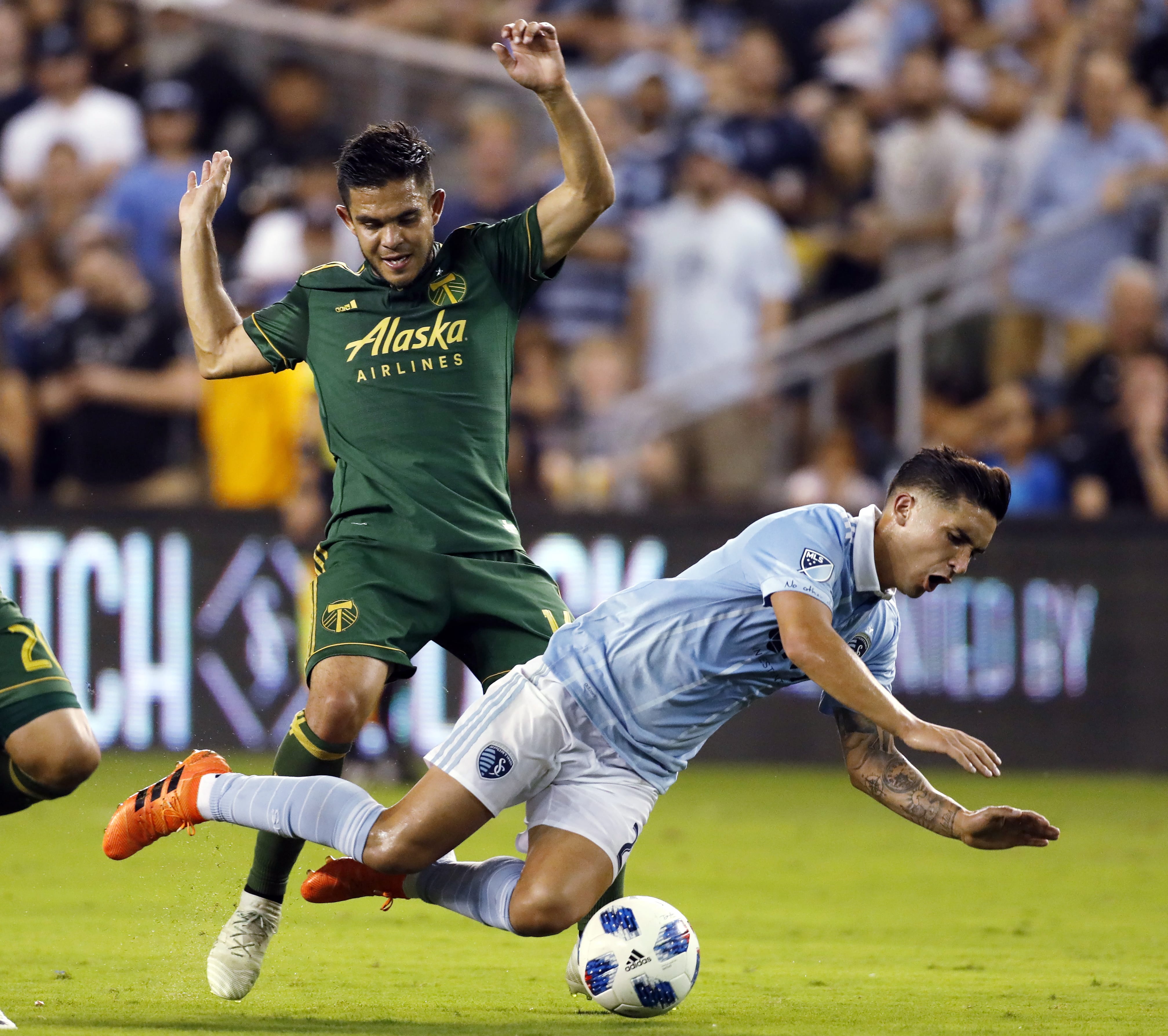 Sporting Kansas City midfielder Felipe Gutierrez, right, is tripped by Portland Timbers midfielder Andres Flores, left, during the second half of an MLS soccer match in Kansas City, Kan., Saturday, Aug. 18, 2018. (AP Photo/Colin E.