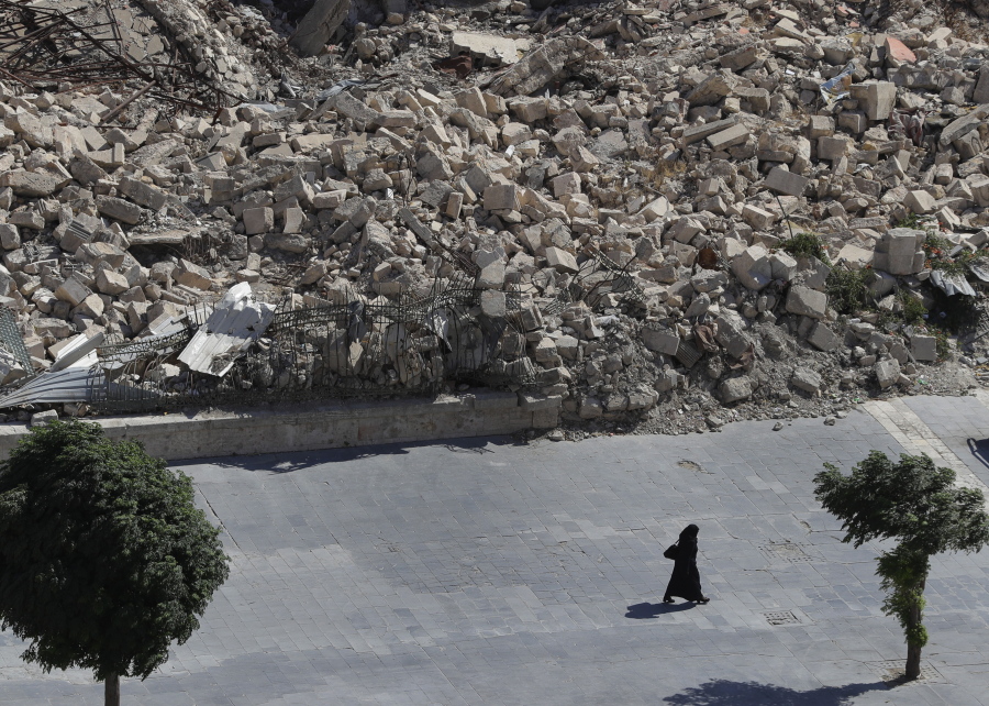 In this photo taken on Thursday, Aug. 16, 2018, a woman walks past the remnants of destroyed buildings in the city of Aleppo, Syria. Russian air defense assets in Syria claim to have downed 45 drones targeting their main base in the country, its military said Thursday, after an attack by the Islamic State group on a Syrian army base a day earlier killed seven troops.