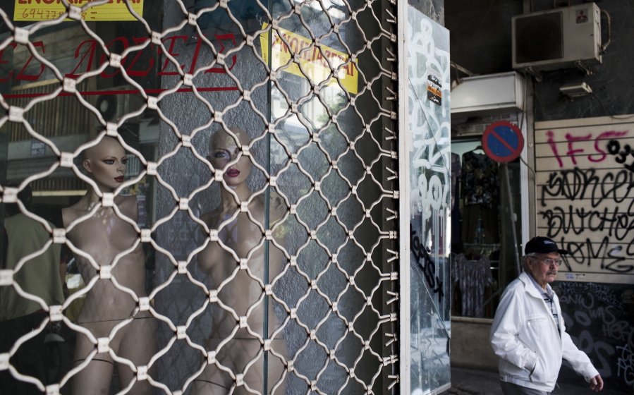 FILE - In this file photo dated Monday, May 22, 2017, mannequins stand inside a shuttered shop with signs that read “for rent” as a man walks past in central Athens. Greece officially emerges from its bailout program on upcoming Monday, Aug. 20, 2018, after eight years of cutbacks enforced in return for three massive loan infusions, but the huge debt pile in Greece and throughout Europe could take generations to defuse.