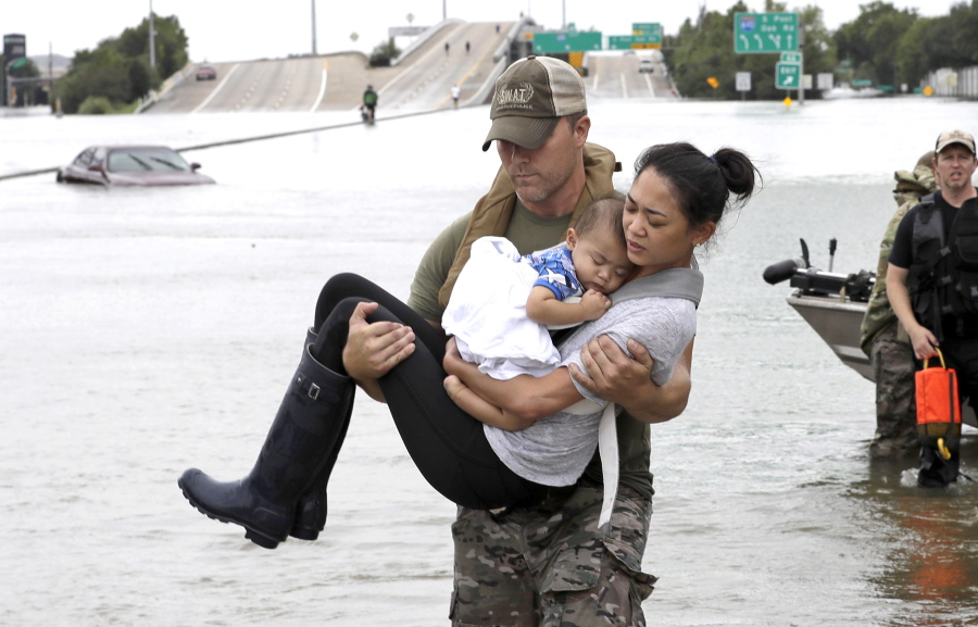 FILE - In this Aug. 27, 2017 file photo, Houston Police SWAT officer Daryl Hudeck carries Catherine Pham and her 13-month-old son Aiden, asleep in her arms, after rescuing them from their home surrounded by floodwaters from Tropical Storm Harvey in Houston, Texas. Hurricane Harvey roared onto the Texas shore nearly a year ago, but it was a slow, rainy roll that made it a monster storm. Federal statistics show some parts of the state got more than 5 feet of rain in five days. Harvey killed dozens and swamped a section of the Gulf Coast that includes Houston, the nation’s fourth largest city, causing billions of dollars in damage. (AP Photo/David J.