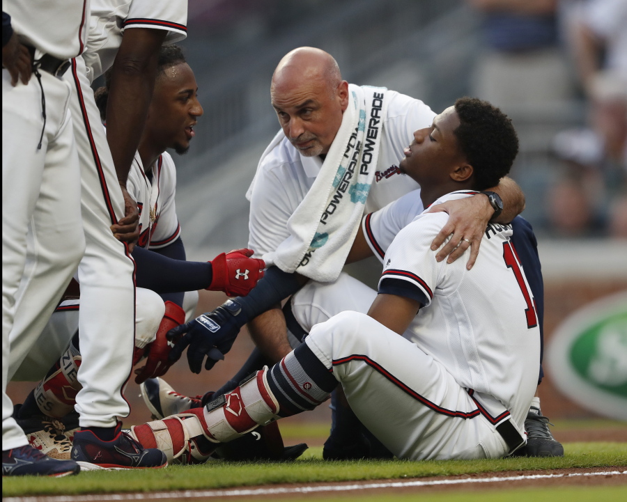 Atlanta Braves’ Ronald Acuna Jr. (13) is tended to by a member of the training staff as Ozzie Albies talks to him after Acuna was hit by a pitch from Miami Marlins starting pitcher Jose Urena during the first inning of a baseball game Wednesday, Aug. 15, 2018, in Atlanta.