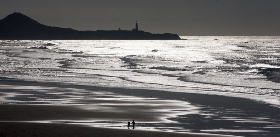 People walk on the beach with the Yaquina Head lighthouse on the horizon in Newport, Ore., Dec. 5, 2011. Randy L.