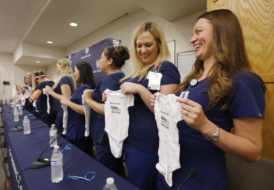 Paige Packard, right, and Allison Thompson, second from right, hold up baby outfits Friday, Aug. 17, 2018, in Mesa, Ariz., as they join most of the sixteen pregnant nurses who work together in the intensive care unit at Banner Desert Medical Center as they attend a news conference as they talk about all being pregnant at the same time, with most of them due to give birth between October and January. (AP Photo/Ross D.
