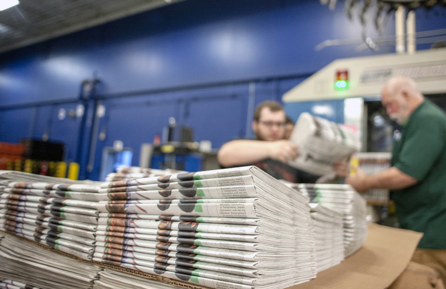 FILE - In this April 11, 2018, file photo, production workers stack newspapers onto a cart at the Janesville Gazette Printing & Distribution plant in Janesville, Wis. The U.S. Commerce Department is going ahead with a tax on Canadian newsprint, a threat to the already-struggling American newspaper industry. The tariffs unveiled Thursday, Aug. 2, are mostly lower than those originally announced earlier this year but would still impose an anti-dumping border tax as high as 16.88 percent.