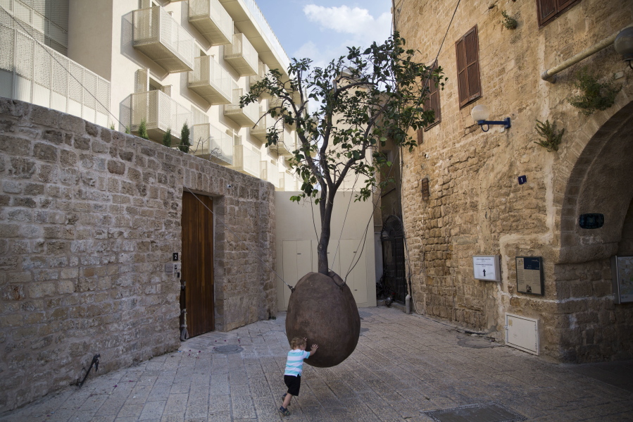 In this Saturday, July 28, 2018 photo, a child plays next to a 100-year-old orange tree hanging above the ground in the old city of Jaffa, Israel. Israel’s port city of Jaffa is an ancient place. Today glass towers and modern apartment complexes rise amid Jaffa’s old white stone buildings. It’s famous for its flea market and hummus cafes. But visitors will also find trendy bars, galleries and boutiques.