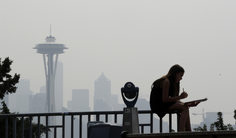 A girl works on a drawing next to an unused viewing scope as a smoky haze obscures the Space Needle and downtown Seattle behind her on Aug. 14.