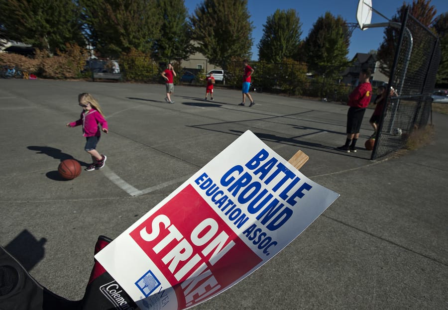 A strike sign is seen as children and teachers play basketball nearby at Marshall Park in Battle Ground on Friday, when striking teachers participated in a variety of community events.