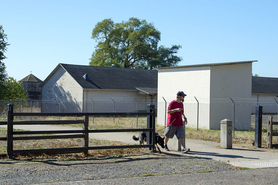 The stockade at Fort Vancouver National Site, left, is obscured by a historical warehouse building Thursday morning as Vancouver resident Greg Martin walks his 6-month-old dog, Sage.
