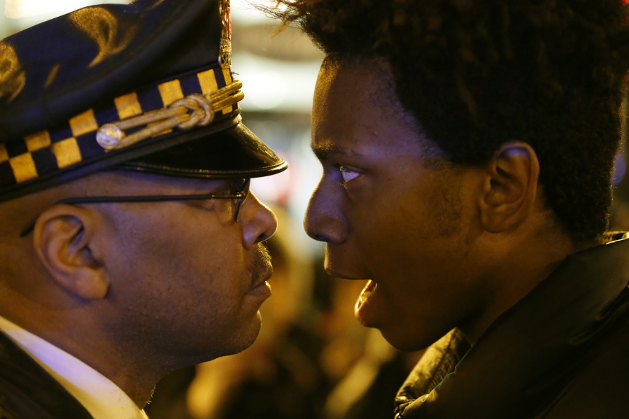 FILE - In this Wednesday, Nov. 25, 2015 file photo, Lamon Reccord, right, stares and yells, "Shoot me 16 times," at a Chicago police officer as he and others march through Chicago's Loop, one day after murder charges were brought against police officer Jason Van Dyke in the killing of 17-year-old Laquan McDonald.