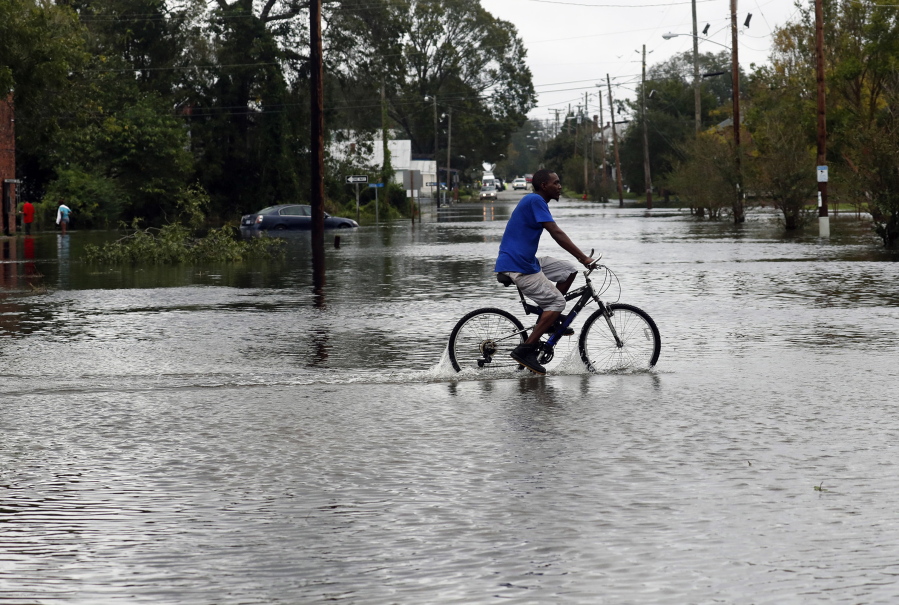 A man rides a bicycle on a street covered by floodwaters caused by the tropical storm Florence in New Bern, N.C., on Saturday Sept. 15, 2018.