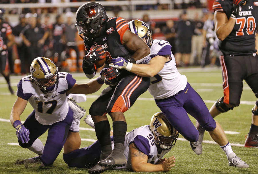 Utah running back Zack Moss (2) is tackled by Washington’s Ben Burr-Kirven (25), Greg Gaines (99) and Tevis Bartlett (17) Saturday in Salt Lake City.