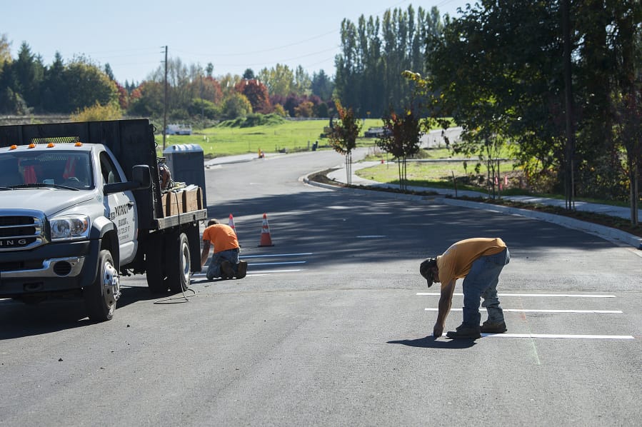 Miguel Martinez of Patriot Sealcoat, Inc., right, helps with the installation of pavement markings in a subdivision under construction south of The Cedars on Salmon Creek on Thursday afternoon.