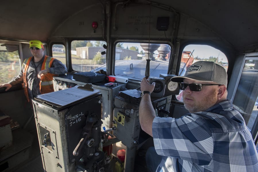 Anthony Hauzenberger, right, of Portland Vancouver Junction Railroad, works with general manager Nathan Bruce as he sounds the horn while traveling over a railroad crossing at Rye rail yard in Vancouver on Wednesday morning.