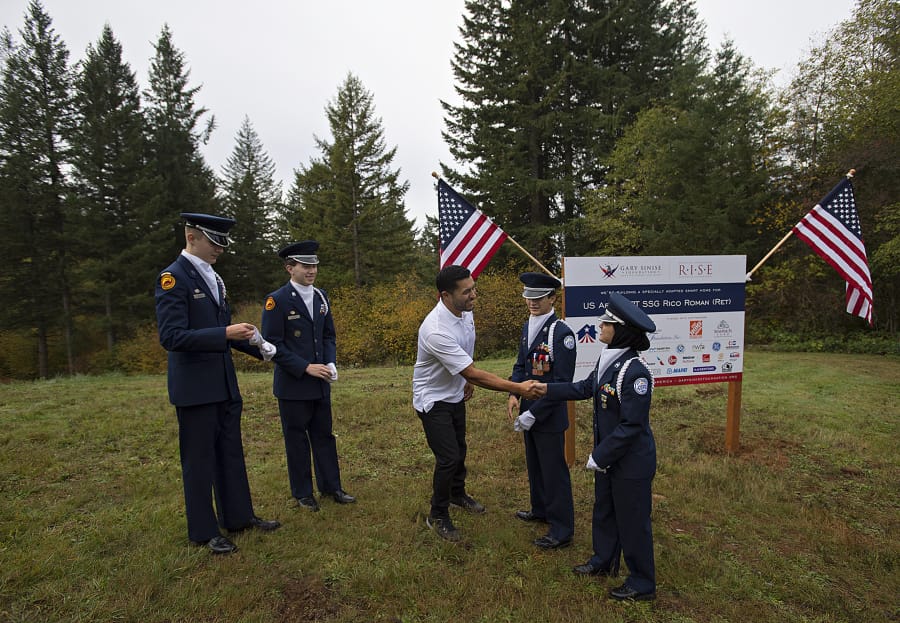 John Snyder, 17, from left, and Nathaniel Garate, 17, both members of the Prairie High School Junior Reserve Officers’ Training Corps, look on as United States Army veteran Rico Roman greets JROTC members Austin Tran, 16, and Ayah Al Baiaty, 17, after the groundbreaking for his new home in Hockinson on Wednesday morning. The Gary Sinise Foundation is building specially adapted smart homes for severely wounded veterans like Roman, who lost his leg while serving his country.