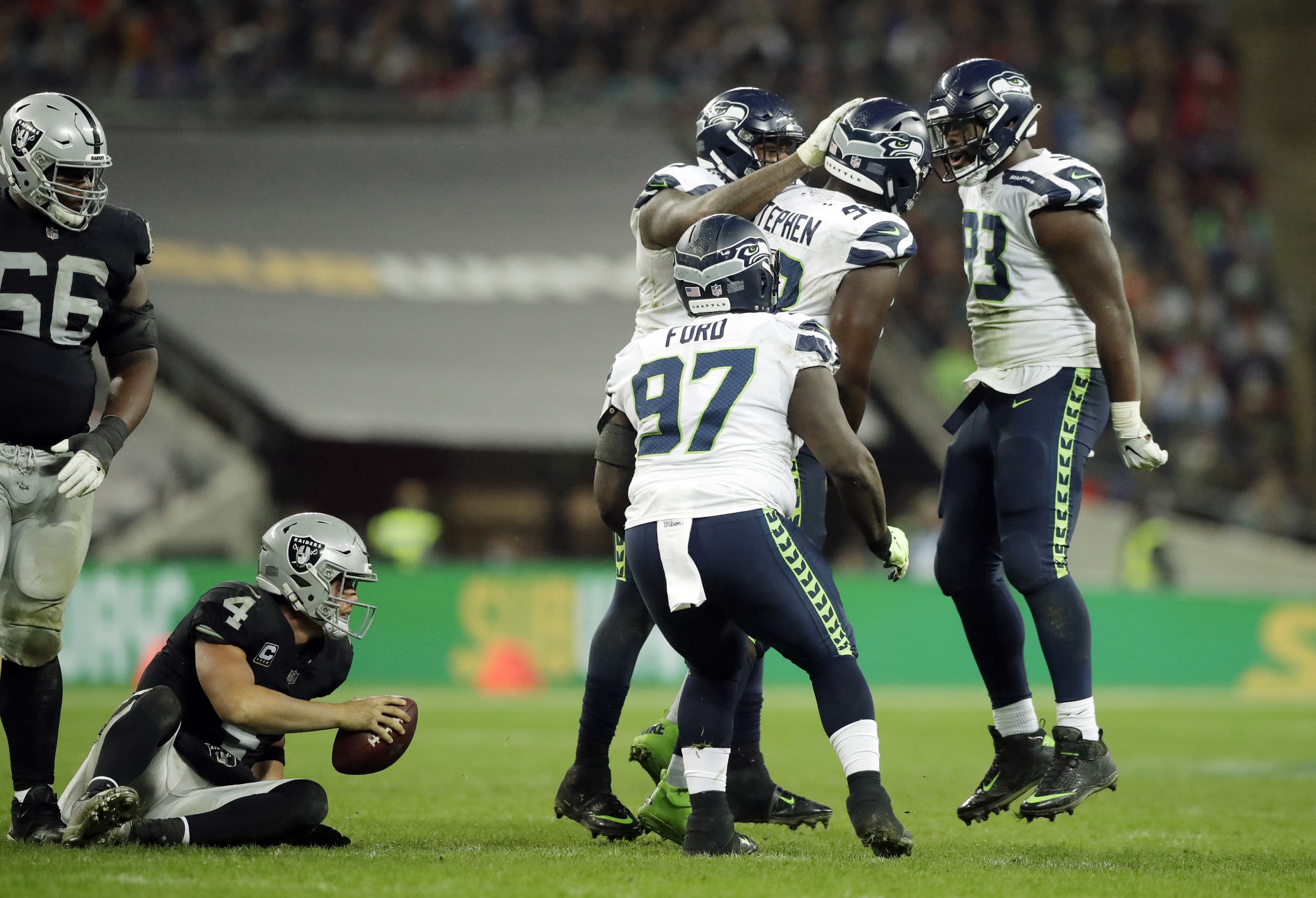 Seattle Seahawks players react after sacking Oakland Raiders quarterback Derek Carr (4), bottom left, during the second half of an NFL football game at Wembley stadium in London, Sunday, Oct. 14, 2018.
