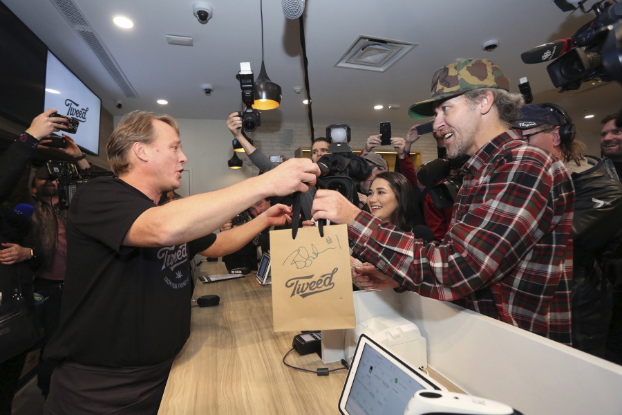 Canopy Growth CEO Bruce Linton, left to right, passes a bag with the first legal cannabis for recreation use sold in Canada to Nikki Rose and Ian Power at the Tweed shop on Water Street in St. John’s N.L. at 12:01 am NDT on Wednesday Oct. 17, 2018.