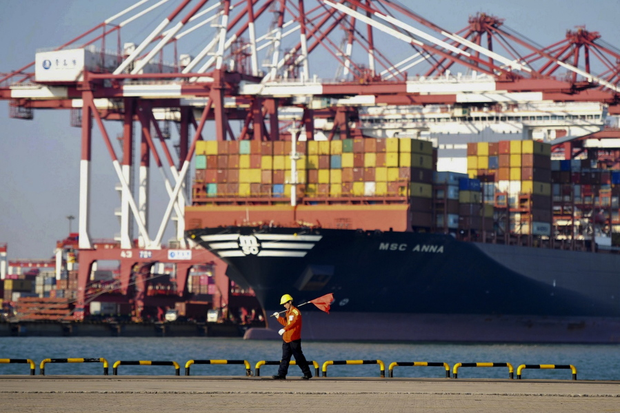In this Friday, Oct. 12, 2018, photo, a worker walks by the container ship docked at a port in Qingdao in east China's Shandong province. China's economic growth slowed further in the latest quarter, adding to challenges for communist leaders who are fighting a mounting tariff battle with Washington.