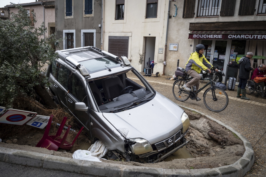 A man rides past a damaged car in the town of Villegailhenc, southern France, Monday.