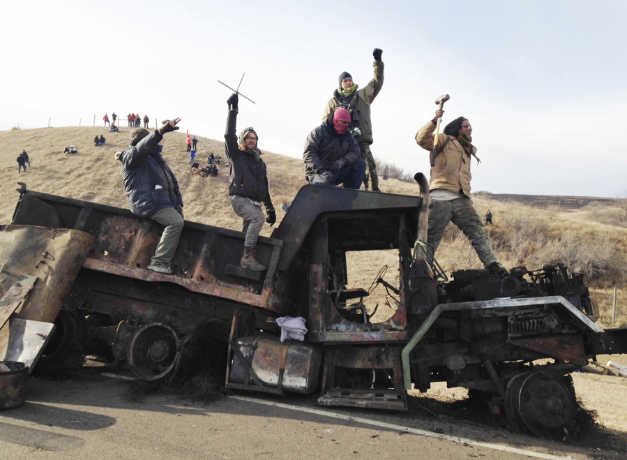 Protesters against the Dakota Access oil pipeline stand on a burned-out truck near Cannon Ball, N.D. In a lawsuit filed, Friday, Oct. 19, 2018, two members of the Standing Rock Sioux tribe and a reservation priest are suing over a five-month shutdown of a North Dakota highway during protests against oil pipeline, saying the closure violated their and others’ constitutional rights.