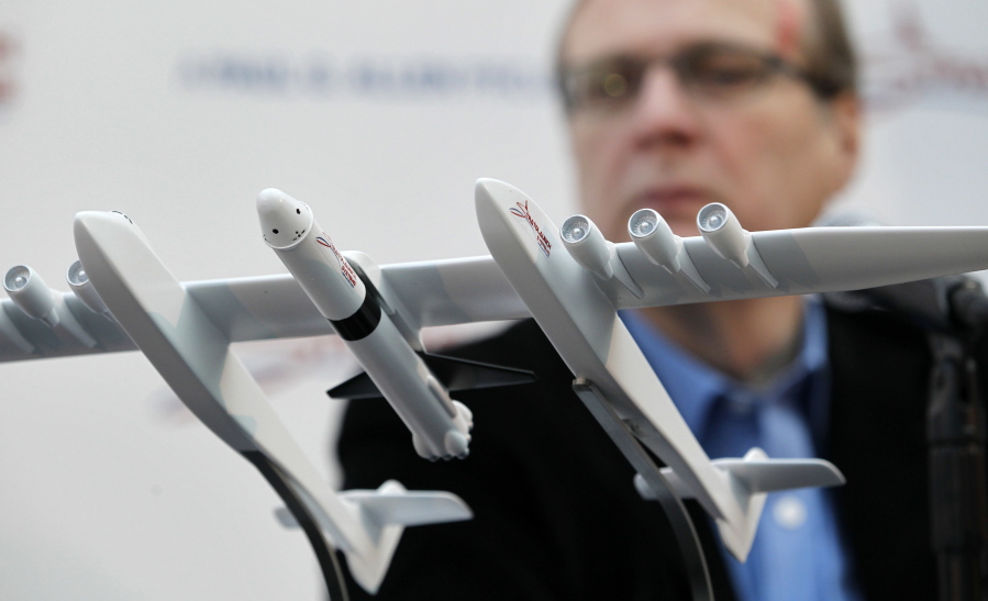 FILE- In this Dec. 13, 2011, file photo Microsoft co-founder Paul Allen looks across at a model of a giant airplane and spaceship he plans on building, during a news conference about the plane in Seattle. Prior to his death on Monday, Oct. 15, 2018, Allen invested large sums in technology ventures, research projects and philanthropies, some of them eclectic and highly speculative. Outside of bland assurances from his investment company, no one seems quite sure what happens now.