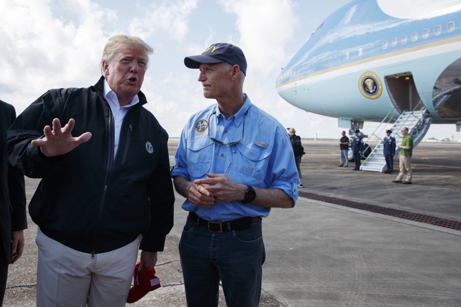 Gov. Rick Scott, R-Fla., right, looks on as President Donald Trump talks with reporters after arriving at Eglin Air Force Base to visit areas affected by Hurricane Michael on Monday in Eglin Air Force Base, Fla.