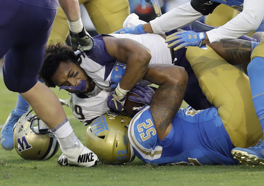 Washington running back Myles Gaskin, top, loses his helmet as he is tackled by UCLA linebacker Lokeni Toailoa (52) during the first half of an NCAA college football game Saturday, Oct. 6, 2018, in Pasadena, Calif.