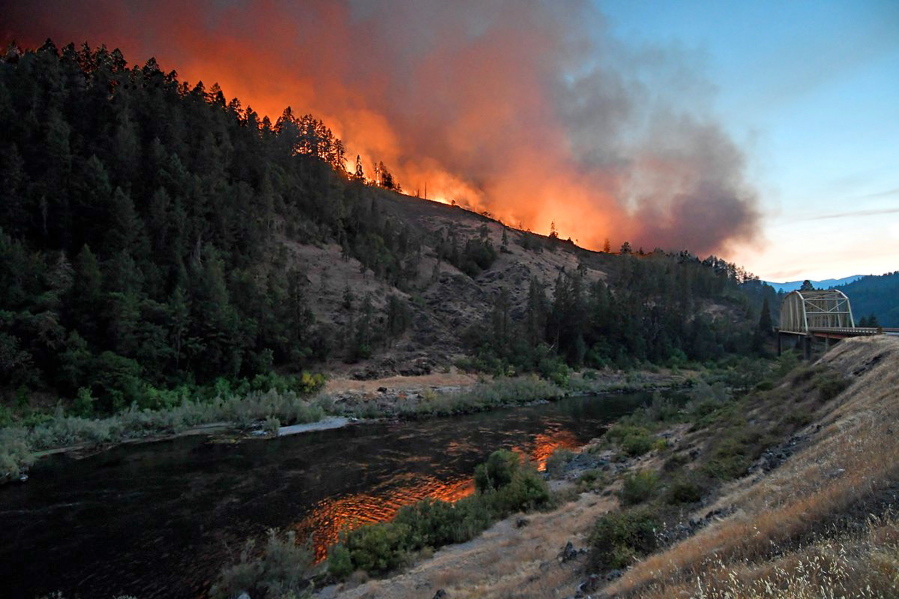 Flames from the Taylor Creek are reflected July 30 in the Rogue River at the Hellgate Bridge near Grants Pass, Ore. New data shows the cost of fighting wildfires in Oregon reached over $500 million in 2018.