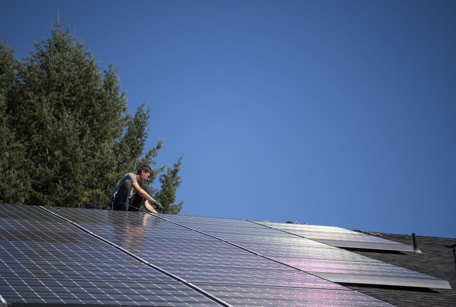 Simon Petersen, roof lead and apprentice electrician at Tesla, wires a solar array on the roof at Mike Burton’s home in September in Vancouver. Burton hopes to connect his solar array to a battery system that will allow him to store power.