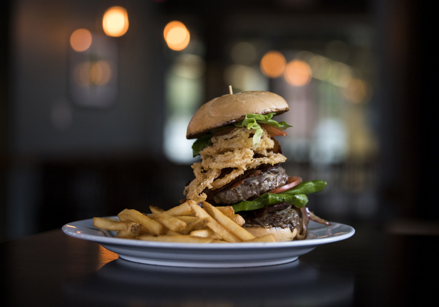 The Double Burger and fries towers over a plate at 2 Rivers Bar and Grill in Washougal. The Double Burger is served with two patties, double bacon, double cheese, caramelized onions, crispy onions, tomato, lettuce and house garlic aioli.