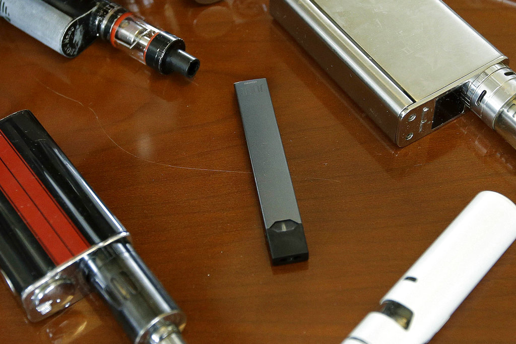 FILE - This Tuesday, April 10, 2018 file photo shows vaping devices, including a Juul, center, that were confiscated from students at a high school in Marshfield, Mass. On Tuesday, Nov. 13, 2018, San Francisco-based Juul Labs Inc. announced it had stopped filling orders for its mango, fruit, creme and cucumber pods but not menthol and mint. It will sell all flavors through its website and limit sales to those 21 and older.