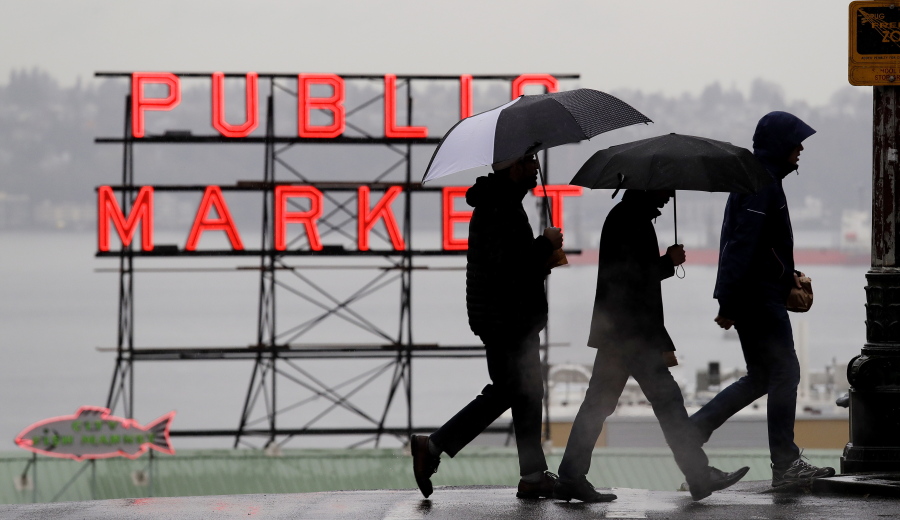 Pedestrians huddle under rain hoods and umbrellas as they pass a sign at the Pike Place Market during a steady rain Monday, Nov. 26, 2018, in Seattle.