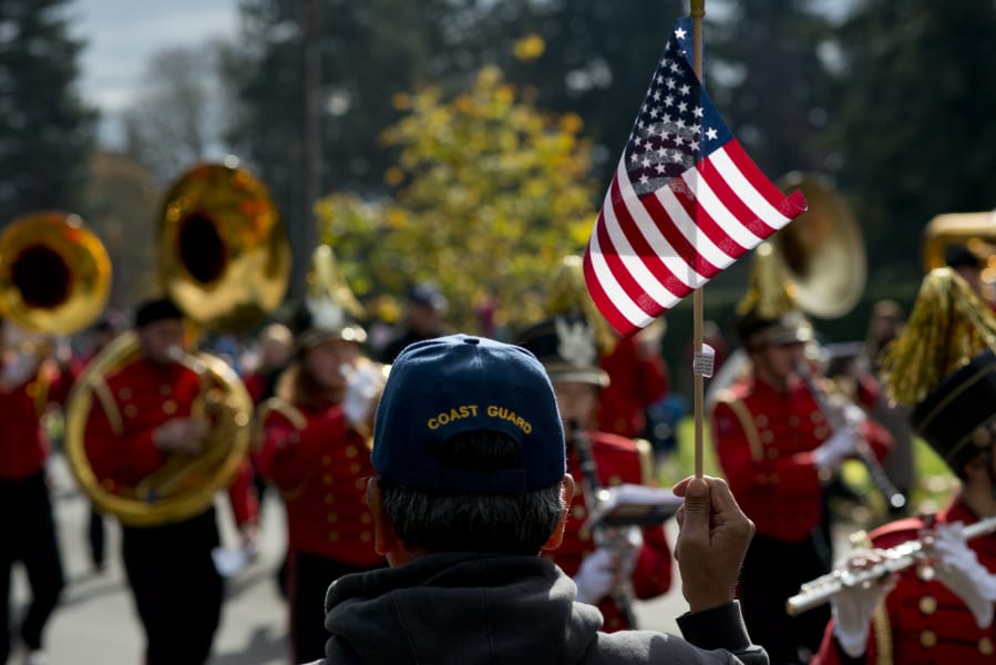 David Medrano, a Vancouver resident and Coast Guard veteran for service from 1972 to 1978, waves a flag as the Camas High School Papermaker Marching Band passes by Saturday in the 32nd annual Lough Legacy Veterans Parade in Vancouver.